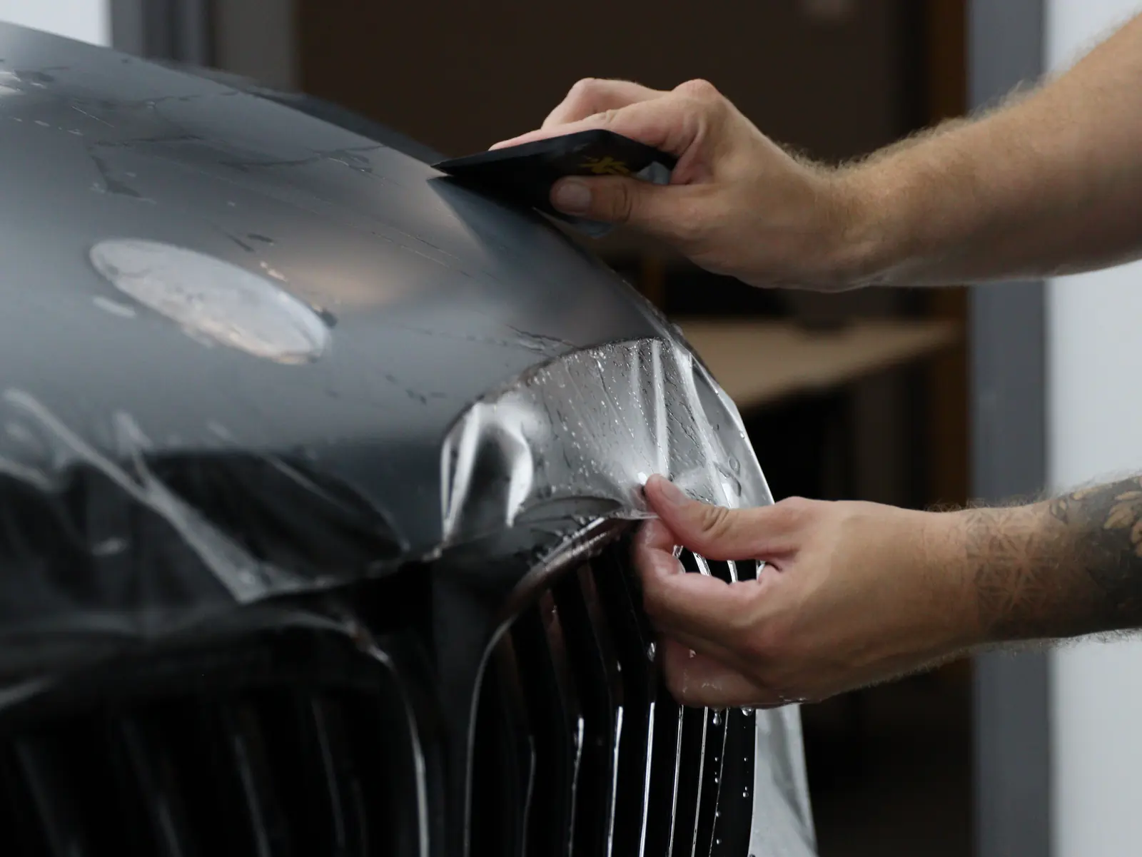 XPEL paint protection film being laid across a black hood at Cobra Auto Styling